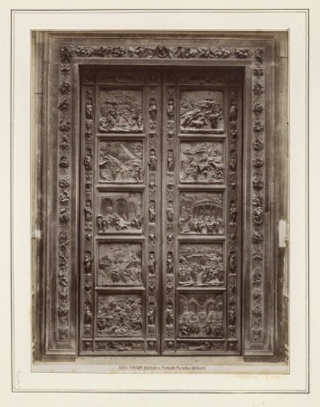 Una fotografía en tonos sepia de grandes puertas de bronce profusamente decoradas y rodeadas por un marco.