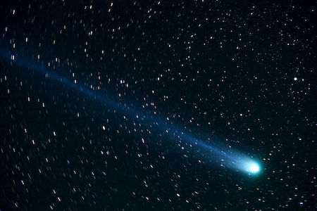 Una fotografía del espacio con muchas estrellas y un cometa azul brillante con una larga cola.