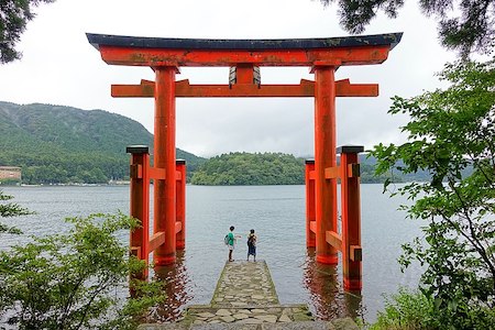 Fotografía de una gran puerta roja abierta frente a un río. Dos personas están de pie debajo de la puerta.