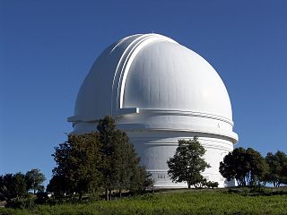 Una fotografía de una gran cúpula blanca contra un cielo azul rodeada de árboles y hierba.