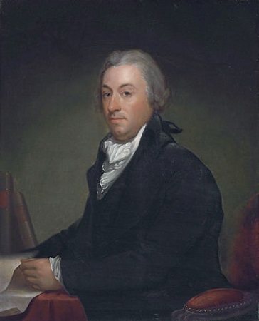 Robert Livingston sostiene un rollo de papel mientras está sentado en una silla roja mirando al espectador.