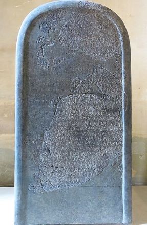 Imagen de piedra moabita. Tiene una parte superior redondeada, coloración manchada (negro/gris) y escritura ilegible.