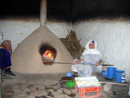 Una fotografía de una mujer sosteniendo un poste y trabajando cerca de un gran horno de barro.