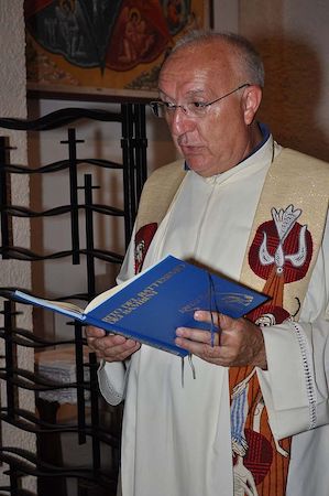 Fotografía en color de un sacerdote sosteniendo un texto religioso y vistiendo vestimentas católicas.