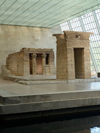 Templo de piedra en exhibición en un museo frente a una pared con ventanas.
