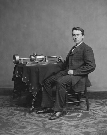 Imagen en blanco y negro de Thomas Edison sentado junto a su fonógrafo