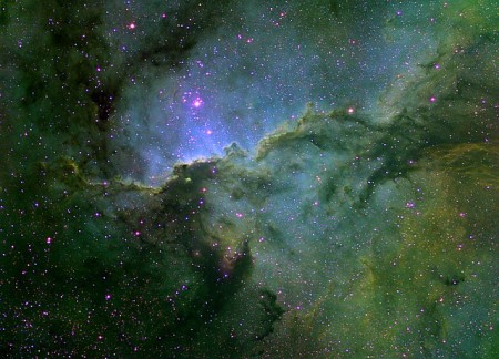 Una nebulosa de emisión con apariencia esmeralda, verde y azul. Nubes moleculares oscuras se extienden como zarcillos.