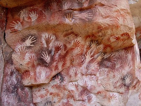 Muchas manos en blanco y rojo en la pared de una cueva
