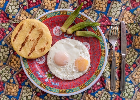 Una imagen de una arepa, con un huevo frito y un poco de okra al lado.