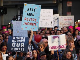 Una gran multitud con carteles en la marcha de las mujeres. Uno dice: Los hombres de verdad veneran a las mujeres.