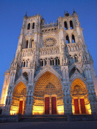 Una imagen del alzado frontal de la catedral de Amiens de noche, con las ventanas iluminadas por la luz.