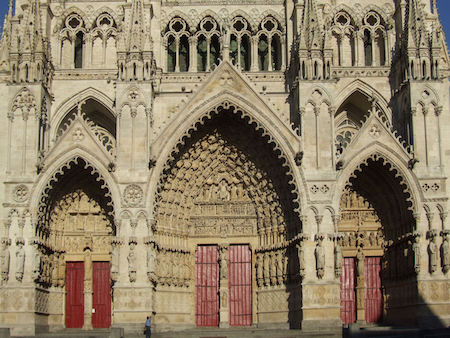 Una imagen del portal de la catedral de Amiens, con tres puertas rojas rodeadas de esculturas de piedra.