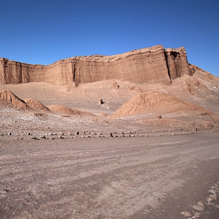La tierra marrón y rocosa conduce a un acantilado color canela en la distancia. El cielo arriba es de un azul profundo y sin nubes.