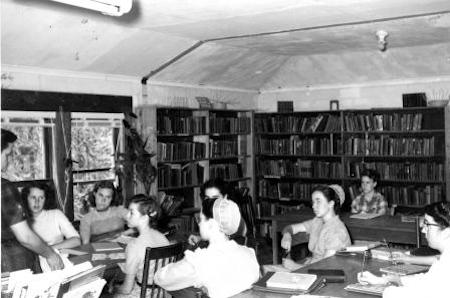 Las estudiantes se sientan en las mesas de la biblioteca de su escuela.