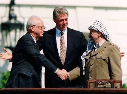 El Primer Ministro de Israel, Rabin (izquierda), le da la mano al líder palestino Arafat (derecha). Presidente de EE. UU. Clinton está detrás/en el centro, con los brazos abiertos.
