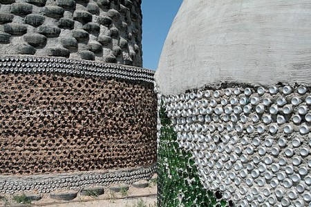 Una pared curva está construida con neumáticos negros y hormigón gris. Otro está construido con latas y hormigón.