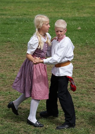 Un niño y una niña rubios bailan afuera mientras usan ropa tradicional