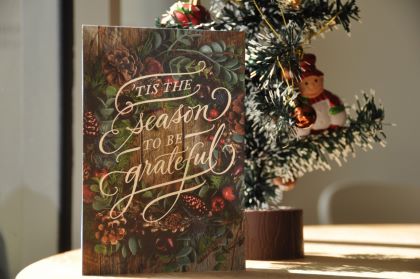 Imagen de una tarjeta navideña sentada frente a un pequeño árbol de Navidad decorativo.