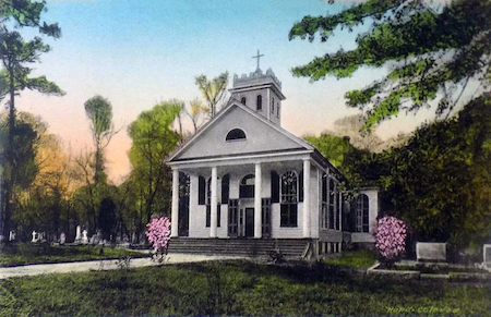 Una fotografía de una pequeña iglesia episcopal rodeada de árboles y un cementerio.
