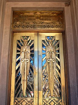Puertas doradas Art Déco con líneas geométricas y figuras alargadas simétricas que sostienen escamas.