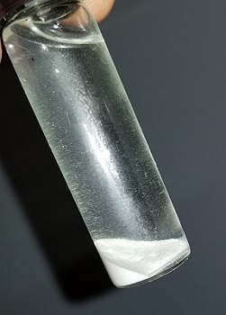 En un tubo de ensayo, hay una acumulación de polvo blanco en el fondo de una solución transparente.