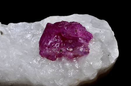 La imagen muestra un cristal de corindón de color violeta rojizo en calcita