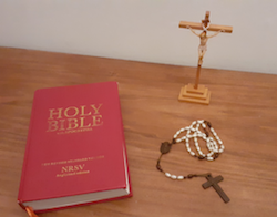 Imagen de un crucifijo, un rosario y la Santa Biblia, todos sobre un escritorio.