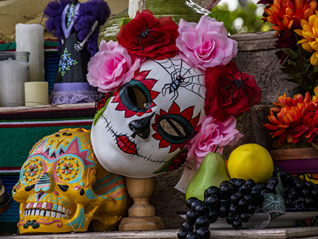 Imagen de máscara y calavera decorada del Día de Muertos rodeada de flores y frutas.