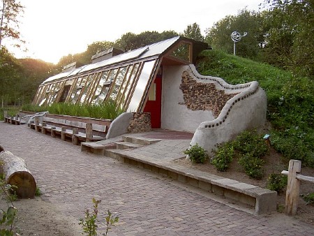 Una casa terrestre con una pared exterior gris con ventanas está construida en una ladera verde.