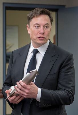 Elon Musk con traje de negocios sosteniendo una réplica de Starship