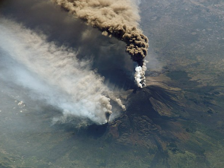 Una vista de pájaro de un volcán en erupción. Está expulsando una columna de ceniza.