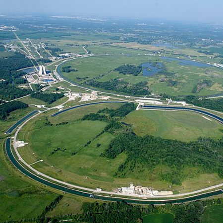 Una vista aérea de estrechos edificios circulares blancos que forman anillos en un paisaje verde y herboso. El cielo es azul.