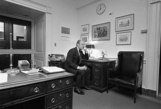 Fotografía en blanco y negro del presidente Gerald Ford hablando por teléfono en su escritorio.