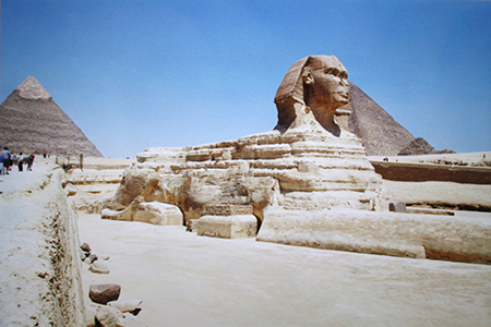Una enorme criatura de piedra con cabeza de faraón y cuerpo de gato se sienta frente a las Grandes Pirámides de Giza.