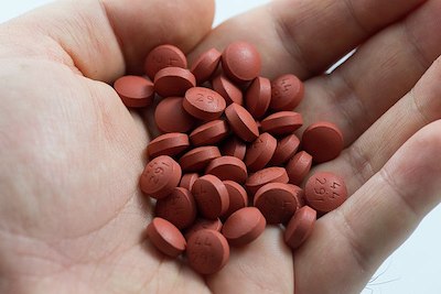 Una fotografía de una mano humana sosteniendo numerosas pastillas rojas y redondas.