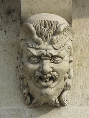 Un primer plano de un mascarón presenta dientes torcidos, un gruñido, ceño fruncido, papada y ojos mirando hacia arriba.