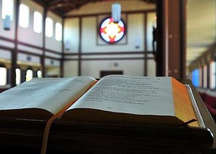 Fotografía de la Biblia abierta en el púlpito de una iglesia con un vitral al fondo