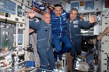 Una fotografía de tres hombres flotando en el compartimento de una abarrotada nave espacial.