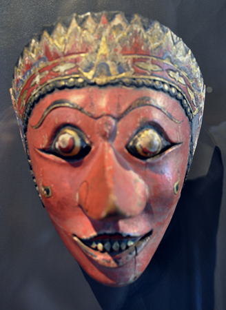 Una máscara de Java con ojos y dientes pintados de oro y un tocado adornado.