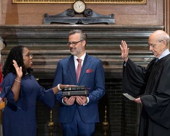 Imagen de una mujer (izquierda) con la mano derecha levantada y la izquierda sobre libros mientras un hombre (derecha) lee su juramento ante la Corte Suprema.