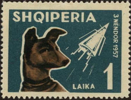 Fotografía en color de un sello con fondo azul, una imagen de Laika a la izquierda y un cohete en la parte superior derecha.