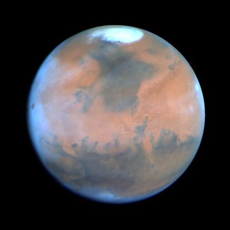 Fotografía en color de Marte que muestra el color rojo del planeta y el casquete polar en la parte superior.