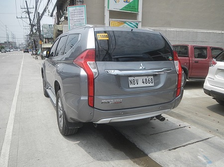 Una foto de la parte trasera de un Mitsubishi Montero gris con vidrios polarizados estacionado al borde de la carretera
