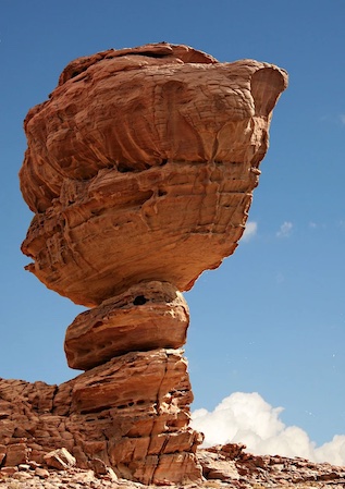 Fotografía de una roca con gran forma esférica en la parte superior sostenida por trozos de roca más estrechos.