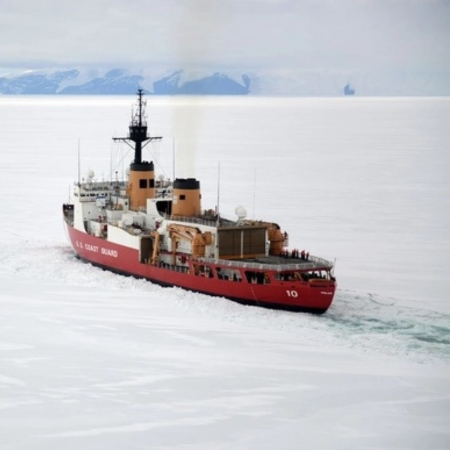 Un barco rojo se mueve a través de aguas blancas y heladas. La tierra azul es visible a lo lejos. El cielo está gris.