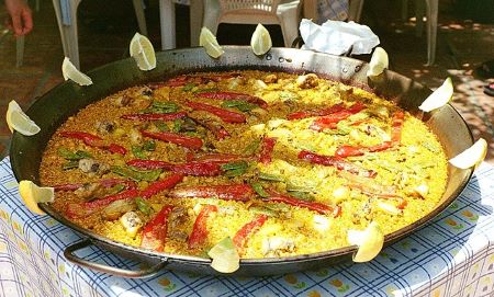 Una sartén grande con arroz amarillo y verduras con rodajas de limón en el borde.