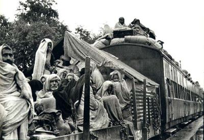Una fotografía en blanco y negro de un tren lleno de gente dentro y fuera de los vagones.