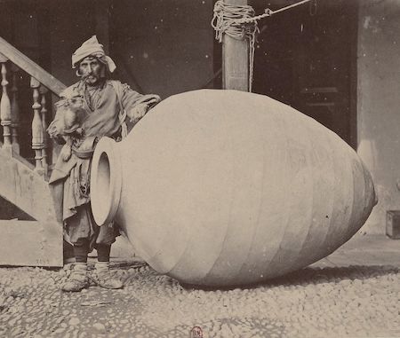 Una fotografía en blanco y negro de un hombre de pie junto a una gran vasija de barro.