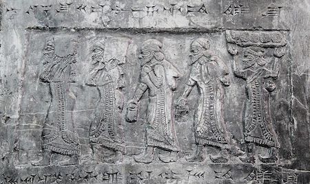 Una talla en bajorrelieve que muestra a cinco hombres de perfil cargando bultos. La escritura cuneiforme rodea la imagen.