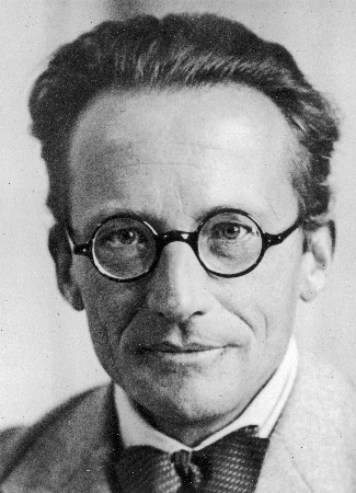 Un retrato en blanco y negro de Erwin Schrodinger. Lleva gafas pequeñas circulares y una pajarita negra.